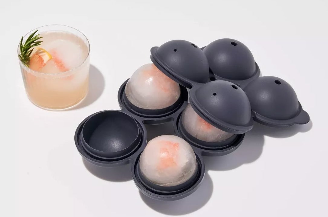 The silicone tray with four spherical molds for the ice cubes and one ice cube in a drink
