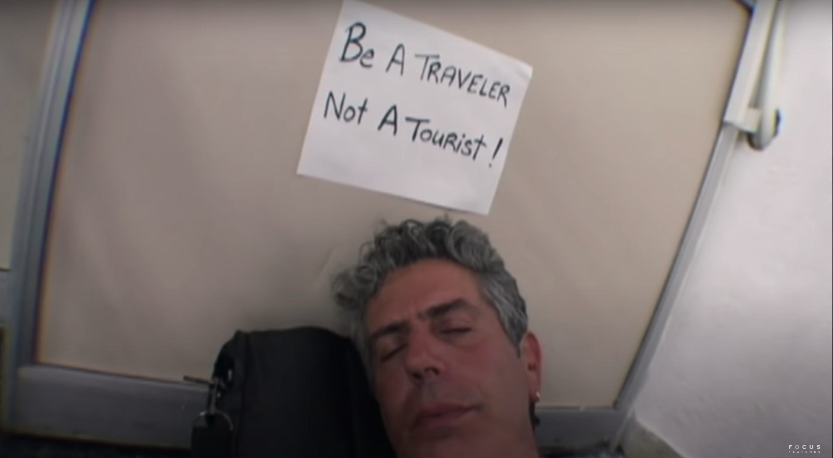 A young Anthony Bourdain snoozes underneath a sign that reads &quot;Be A Traveler, Not A Tourist&quot;