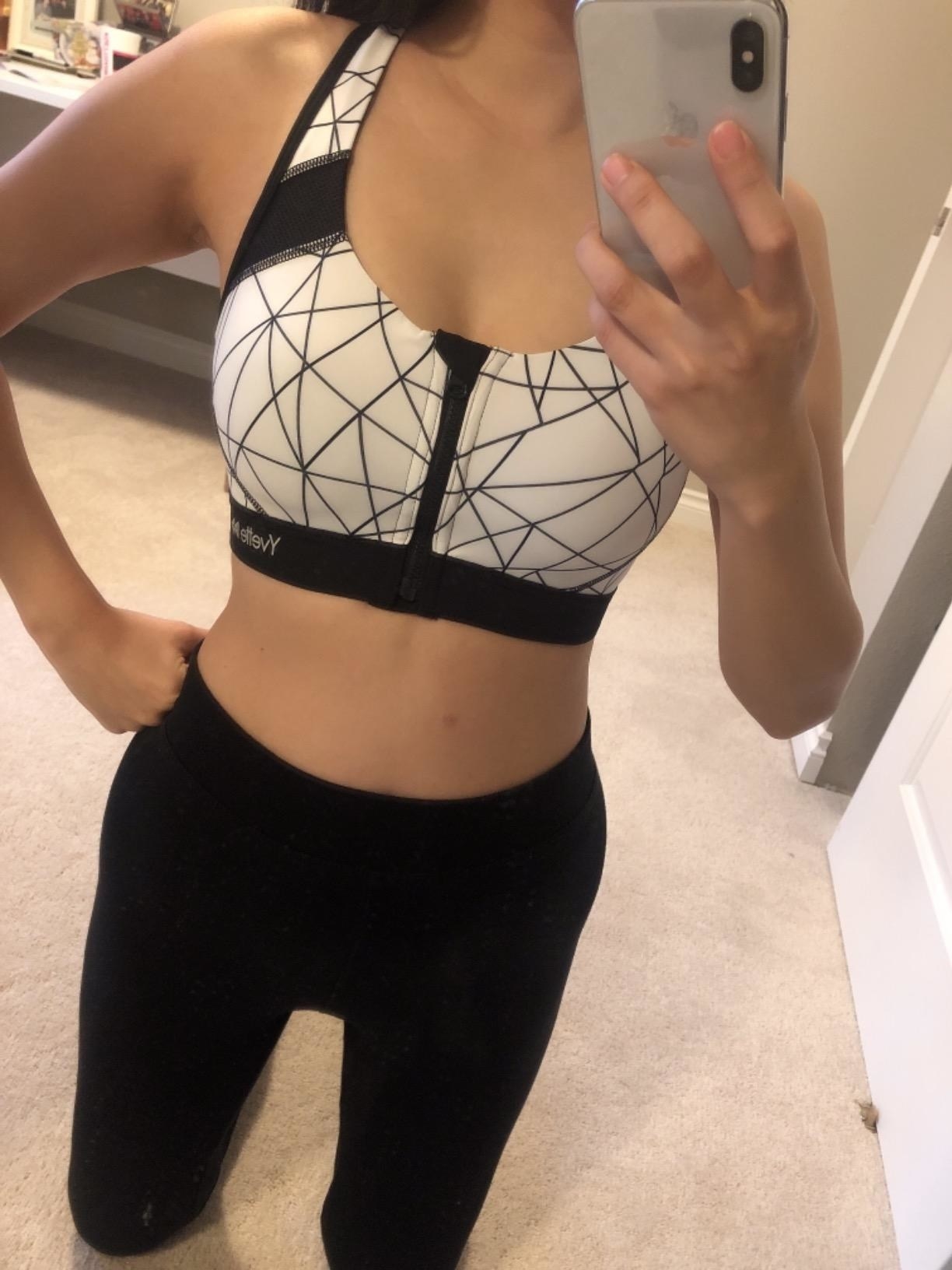 reviewer takes selfie in zip-front black-and-white sports bra and black leggings