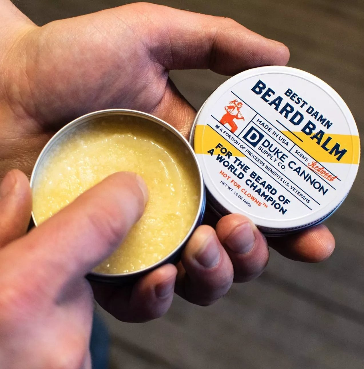 A model putting a finger in the beard balm to show its consistency 