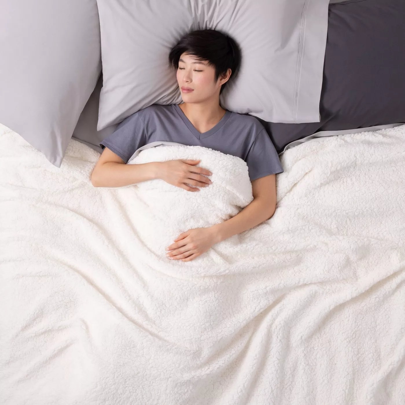 A model sleeping in a bed underneath the fleece blanket