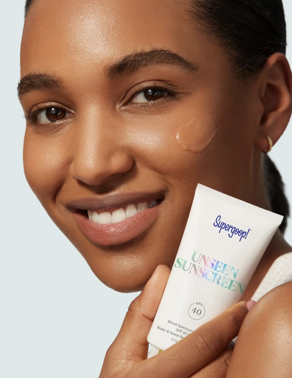 model holding the sunscreen container with a blotch of clear sunscreen on their cheek
