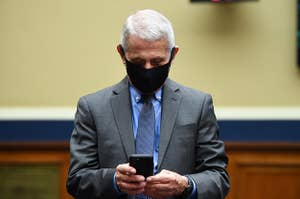 Dr. Fauci, wearing a black mask, looks at his cell phone