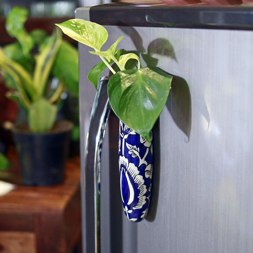 A blue and white planter stuck to a fridge with a plant in it 