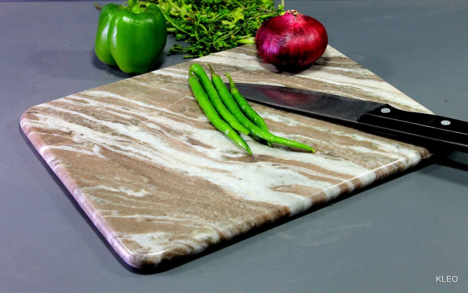 A marble chopping board with chilies, a capsicum, an onion and a knife 
