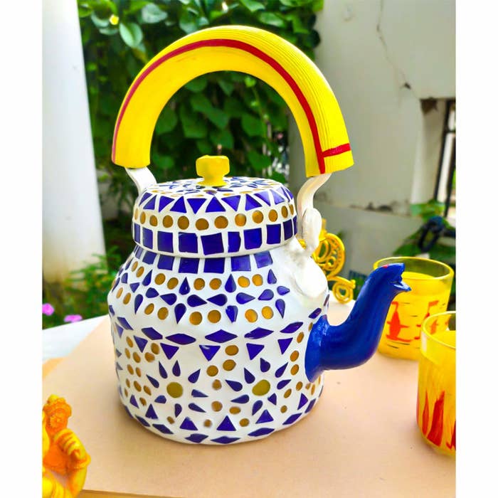 A kettle with blue and yellow mosaic patterns on it next to glasses of orange juice