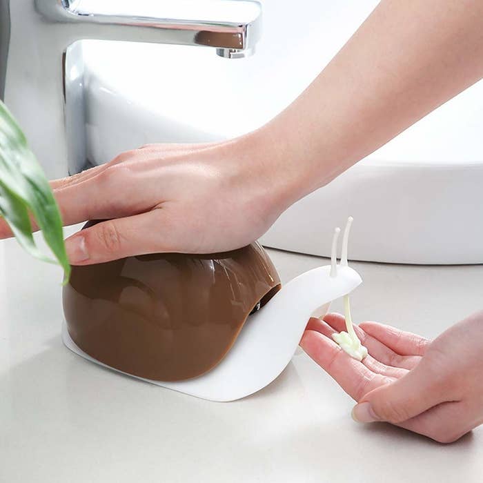 A person squeezing the top of the snail soap dispenser to get soap out of it