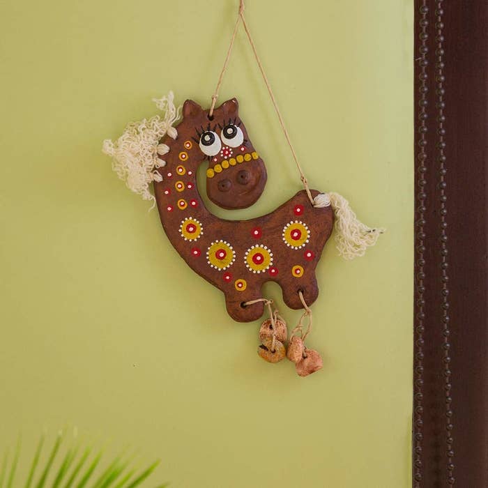 A terracotta horse with bells at the bottom on a wall