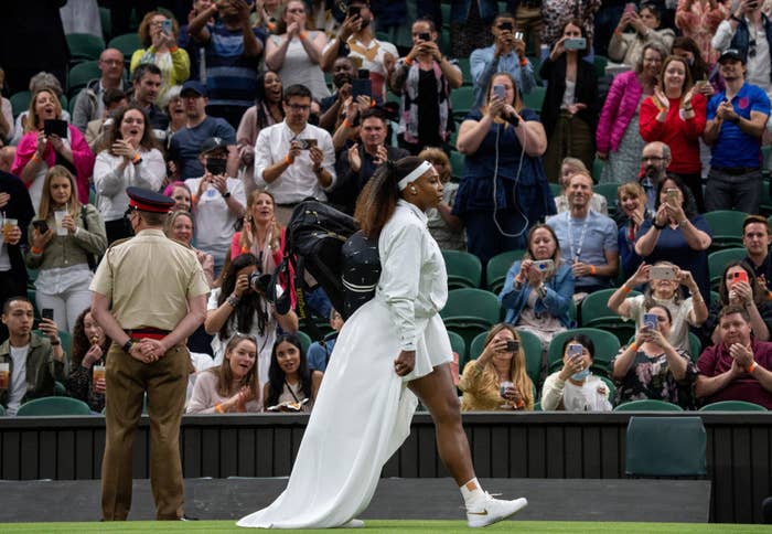 Serena Williams walks on court in a white dress and train before her first-round match at Wimbledon