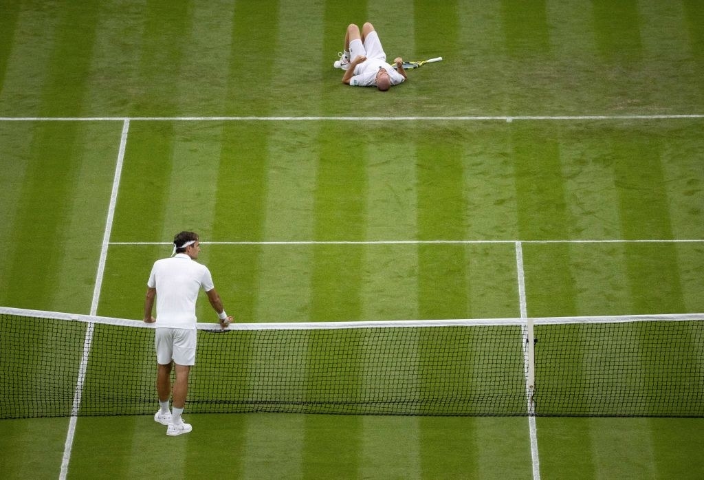 Roger Federer looks on with concern at the net as Adrian Mannarino lies on the ground after slipping on the grass