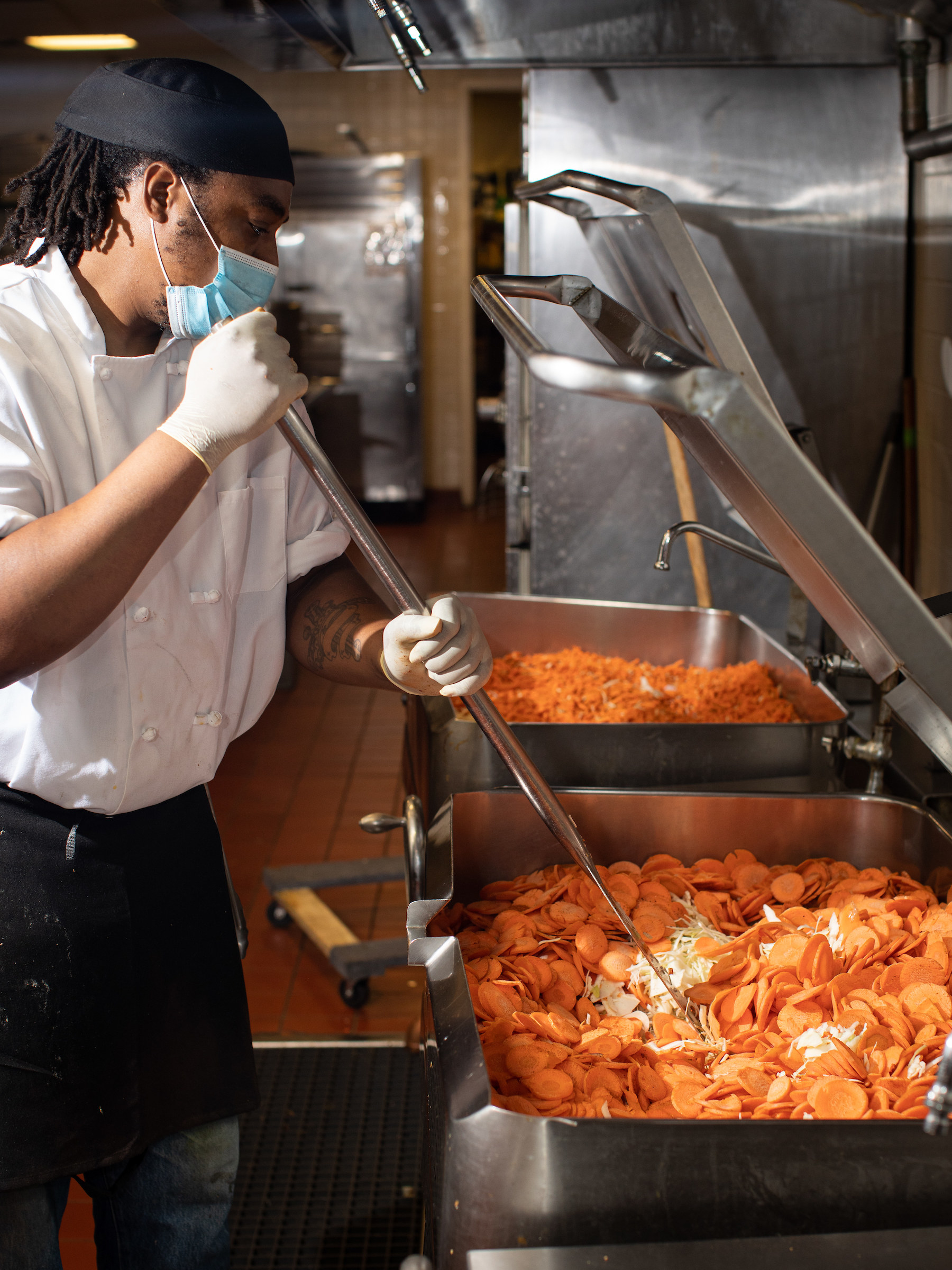 A chef stirs a large pot of food in a restaurant kitchen.