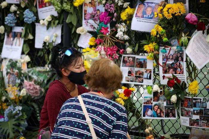 Two people stand in front of a fence covered in flowers and photos