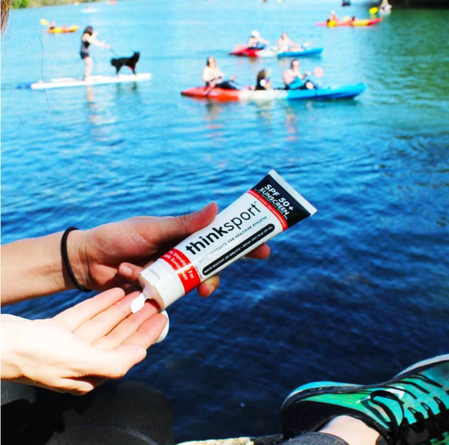 person squeezing sunblock out of a thinksport bottle before going kayaking