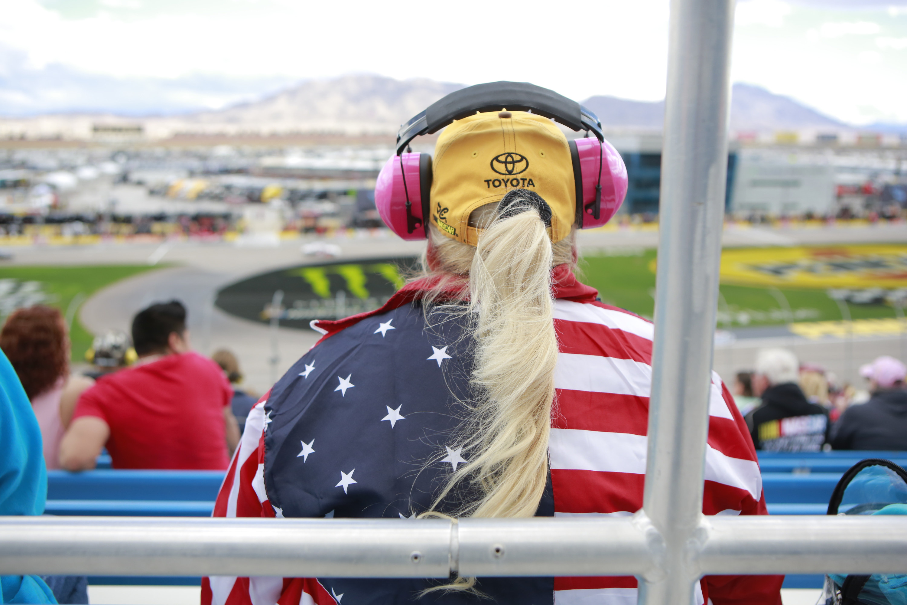 A person wearing an American flag shirt, Toyota cap, and large headphones sits with their back toward the camera