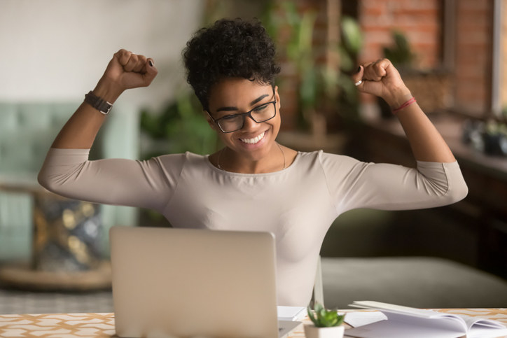 Young woman cheering and smiling in front of a laptop