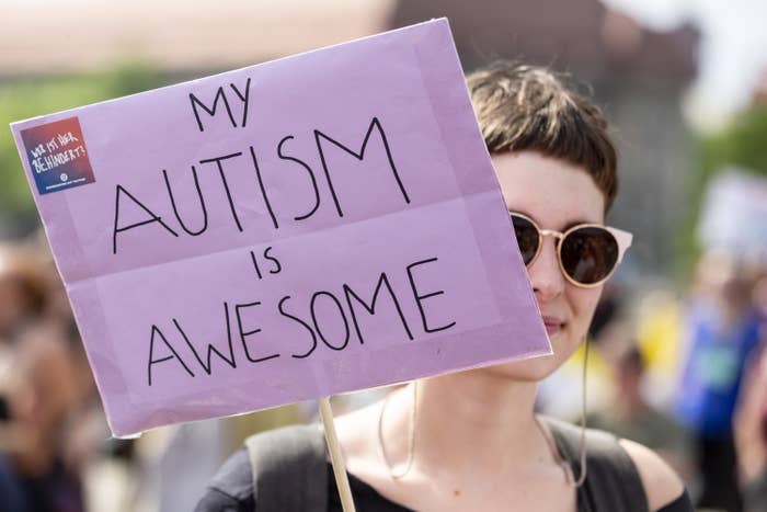 A person at a Pride parade holds a sign that reads &quot;My autism is awesome&quot;