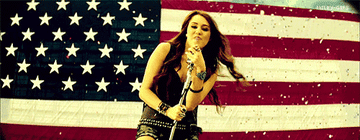 Miley Cyrus singing in front of an American flag
