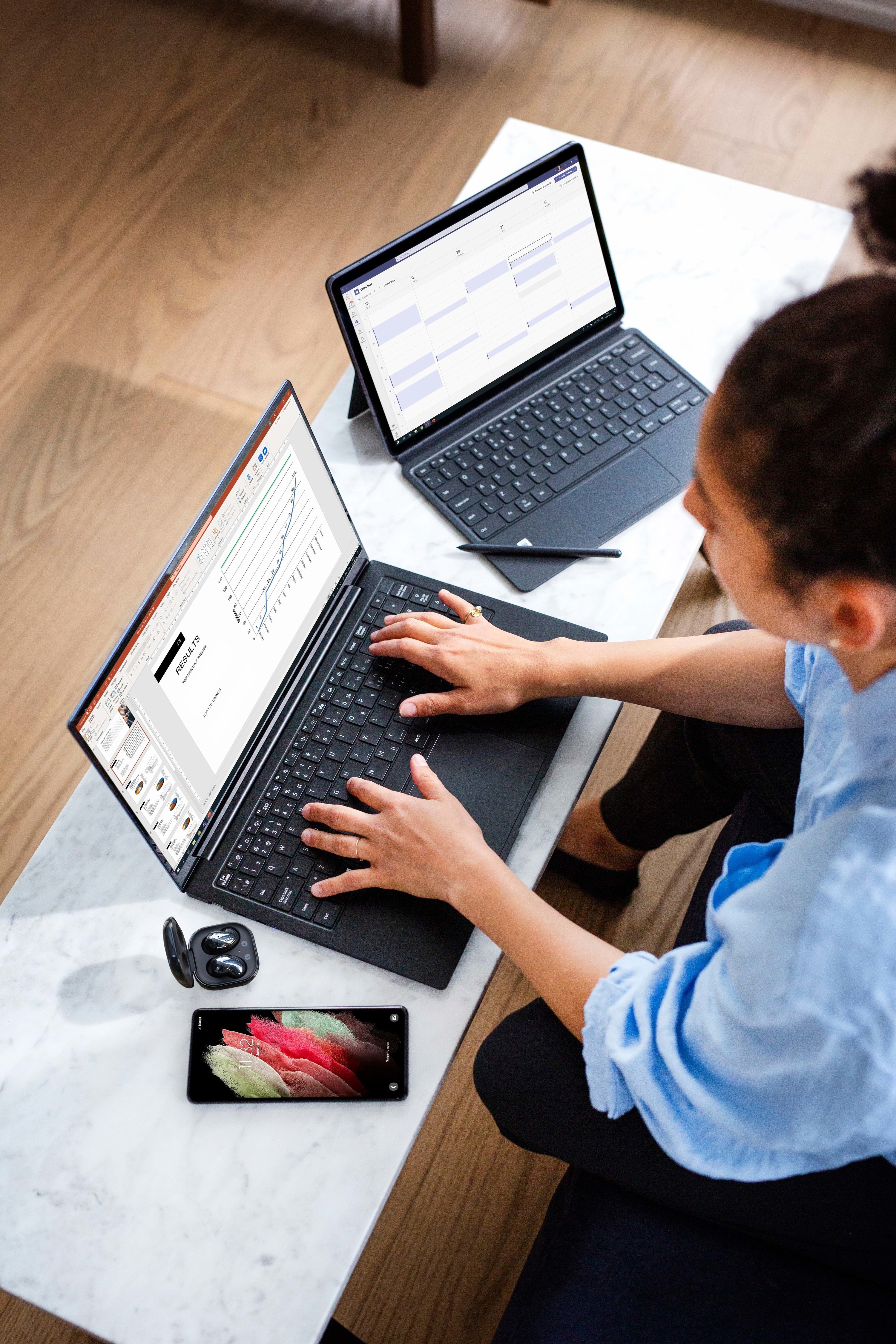 A person typing on the laptop with their phone out