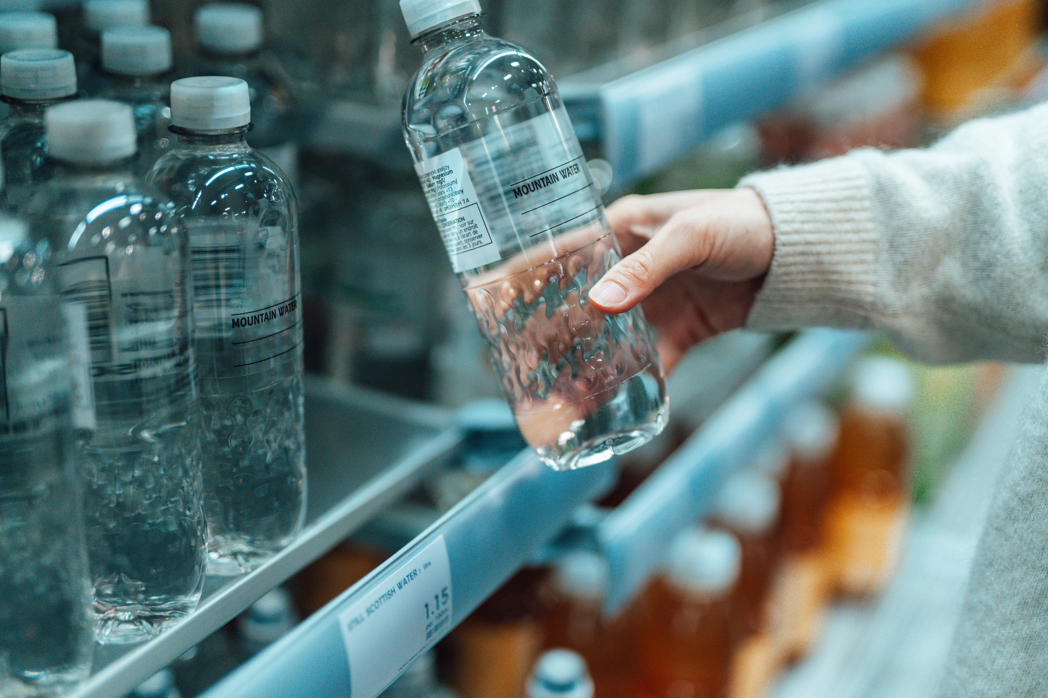 Woman&#x27;s hand picking up a bottle of water in the grocery store