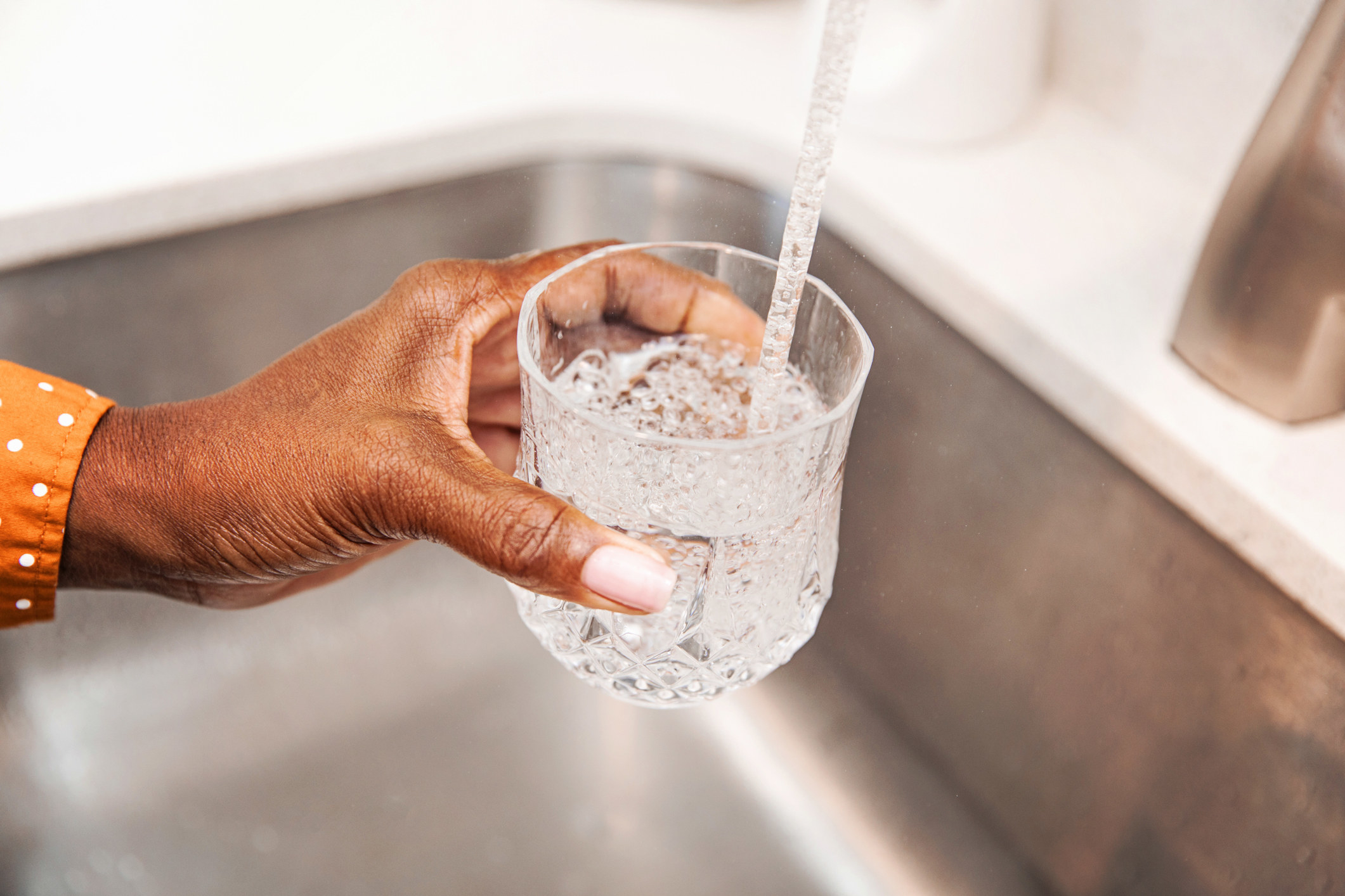 Unrecognizable woman pouring herself a glass of tap water from the kitchen sink