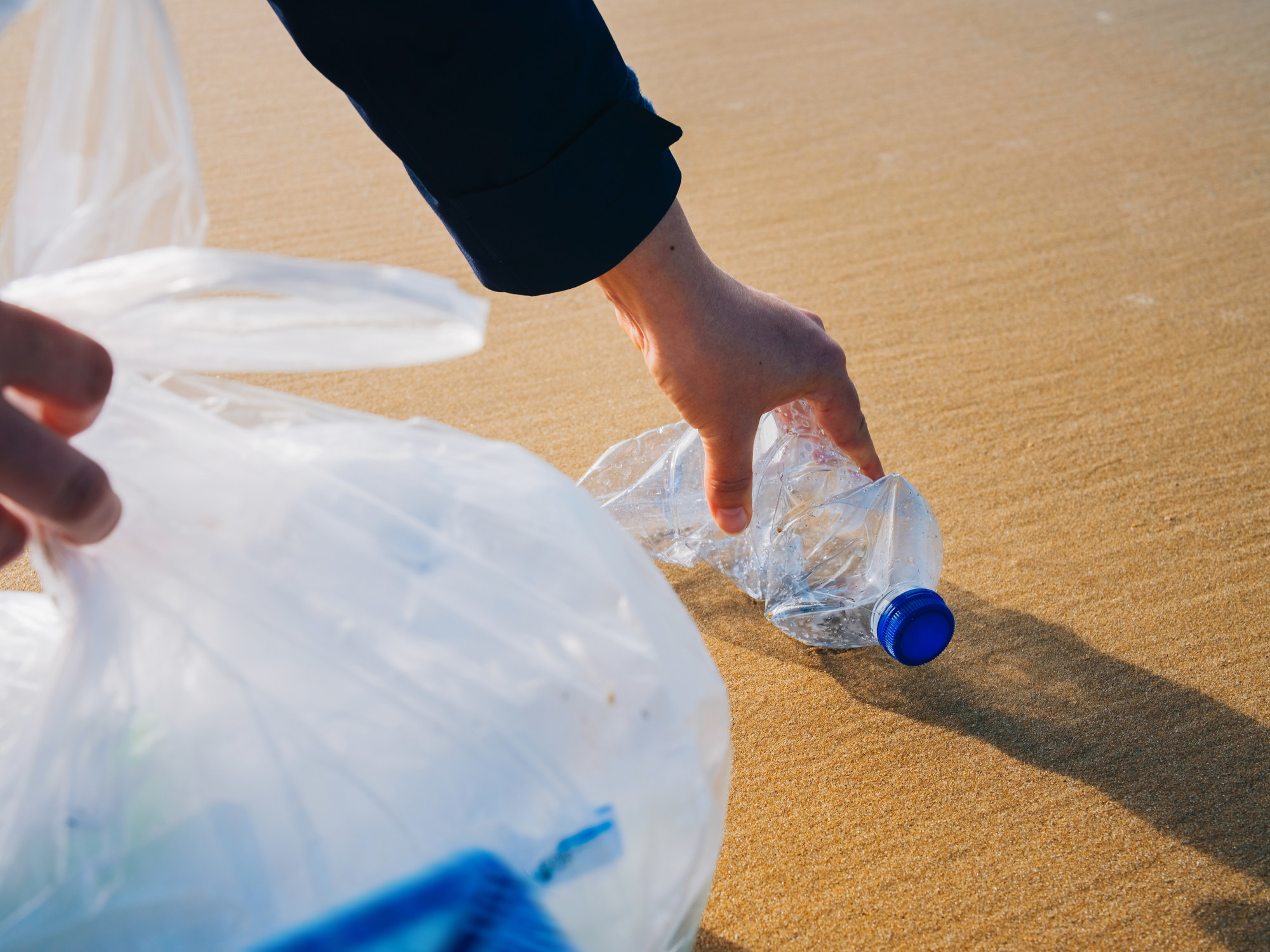 Hand picking up plastic bottle at beach.
