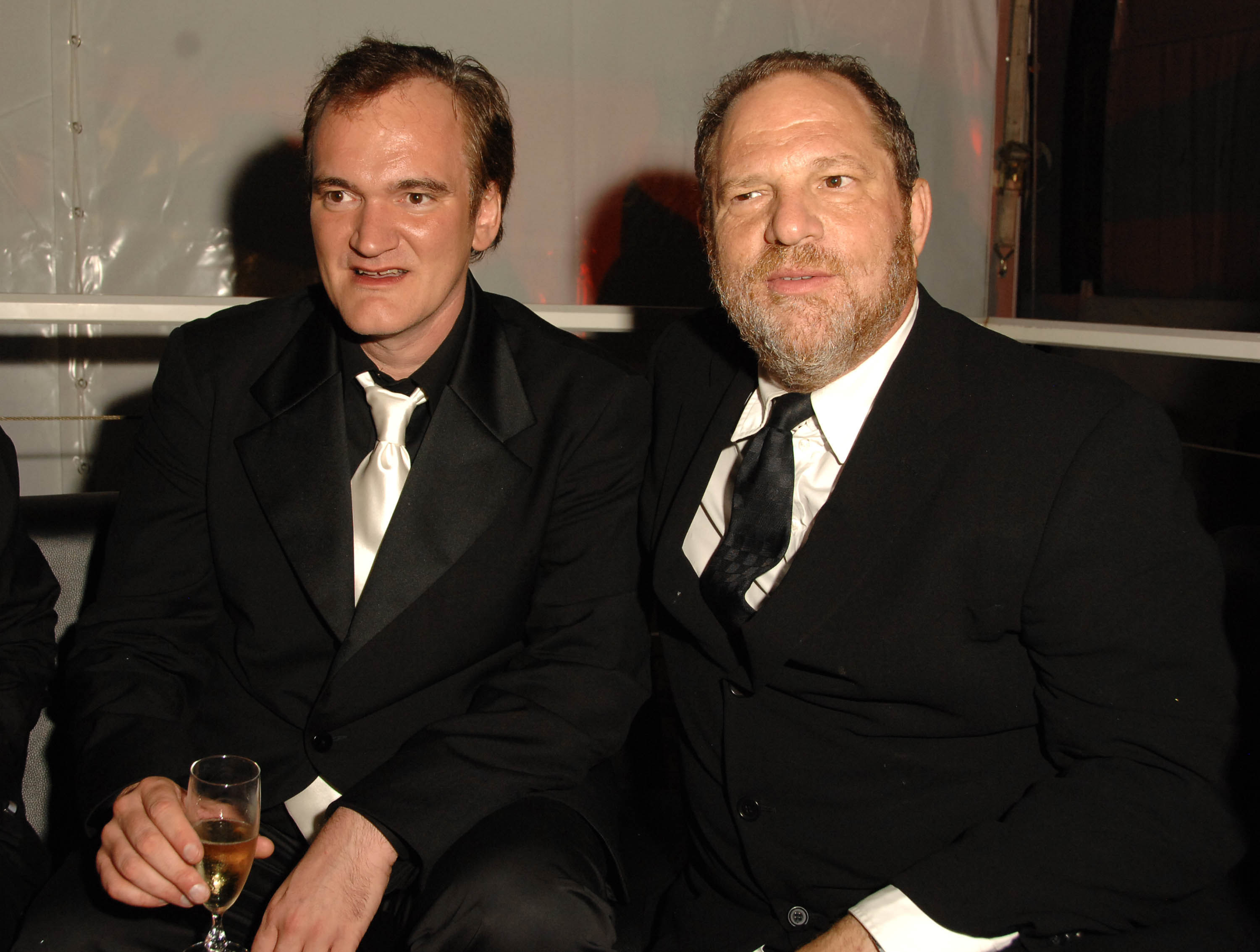 Tarantino holds a glass of champagne while sitting next to Weinstein in 2007
