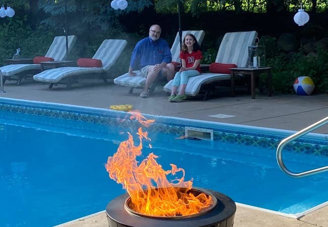 reviewer's lit tiki fire pit next to an in ground pool