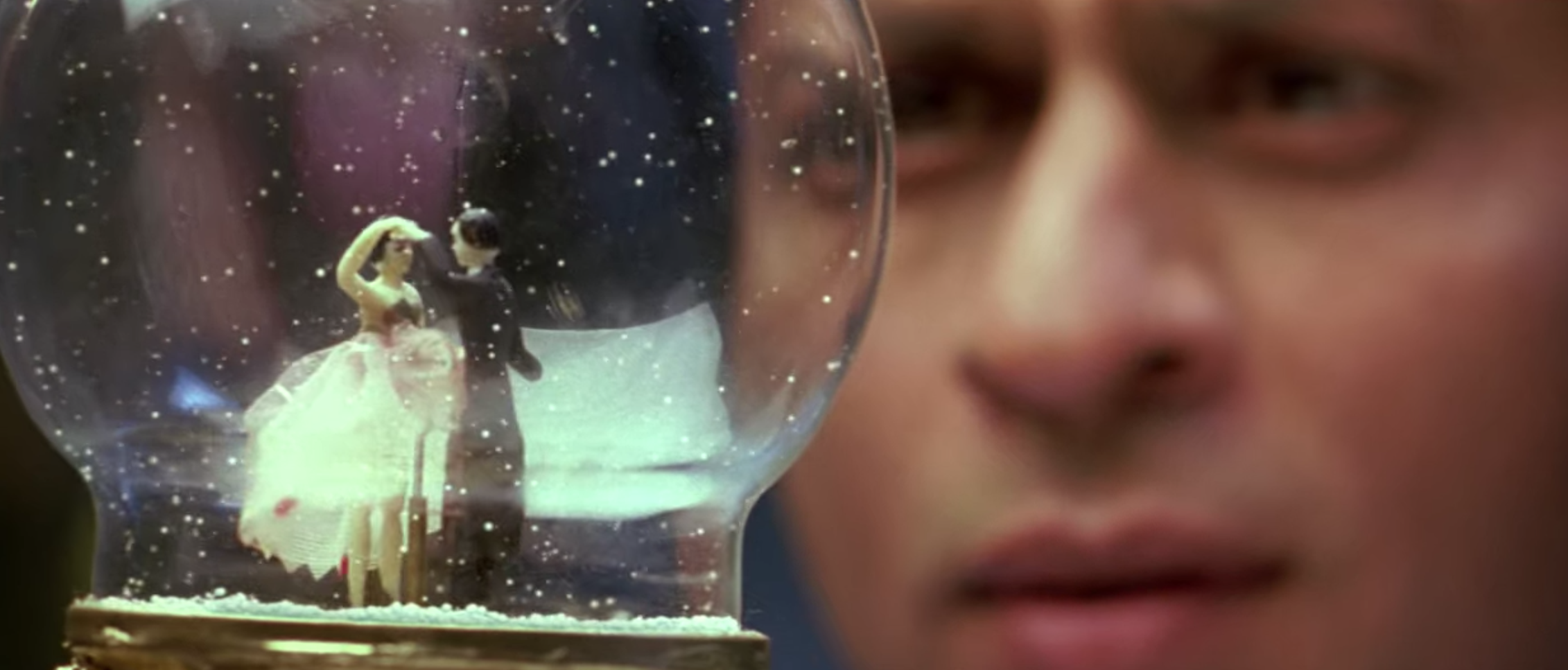 Om gazes into a snow globe which contains a woman and man dancing in the snow.