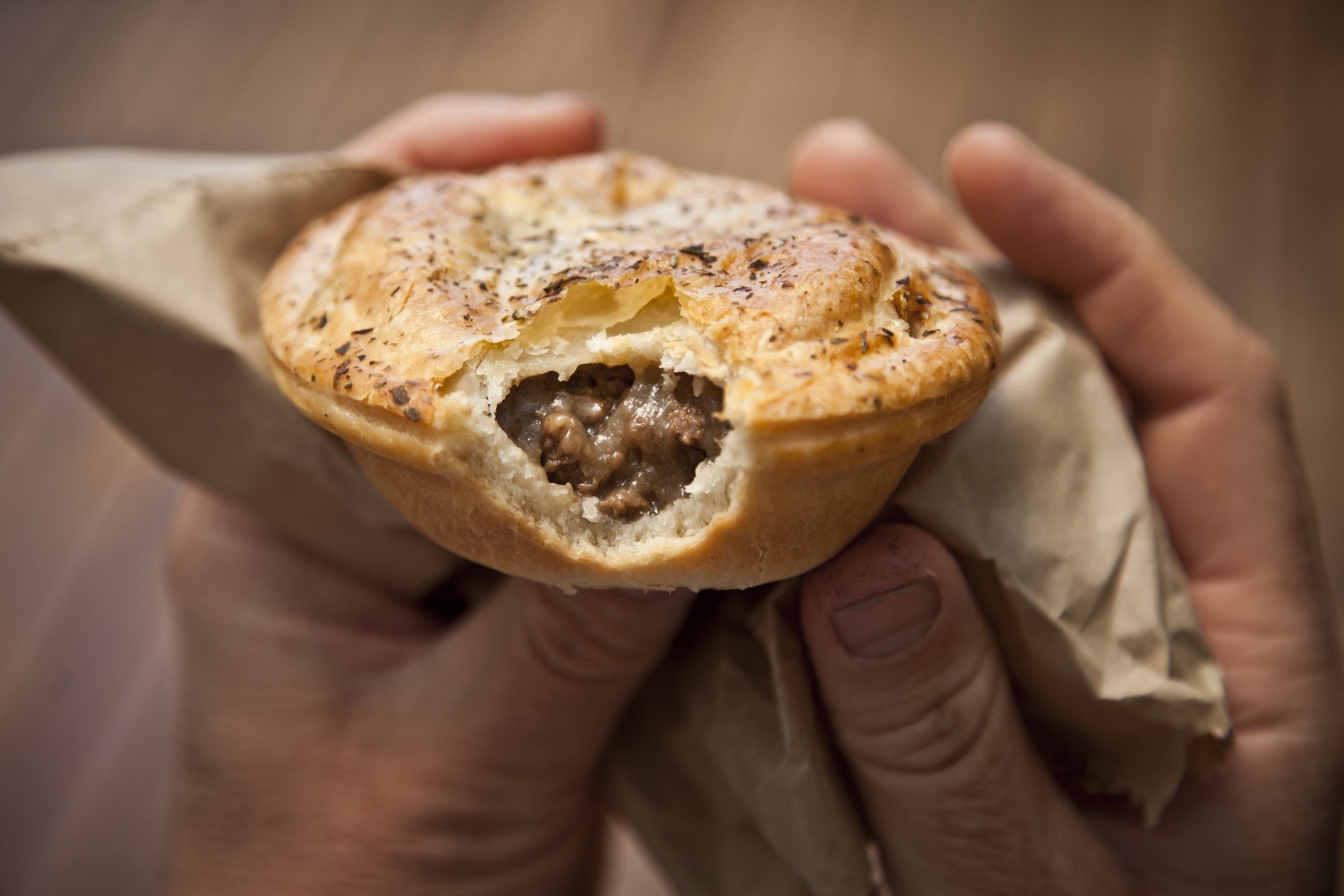 Close-up of a man&#x27;s hands holding an Australian meat pie with a bite taken out of it.