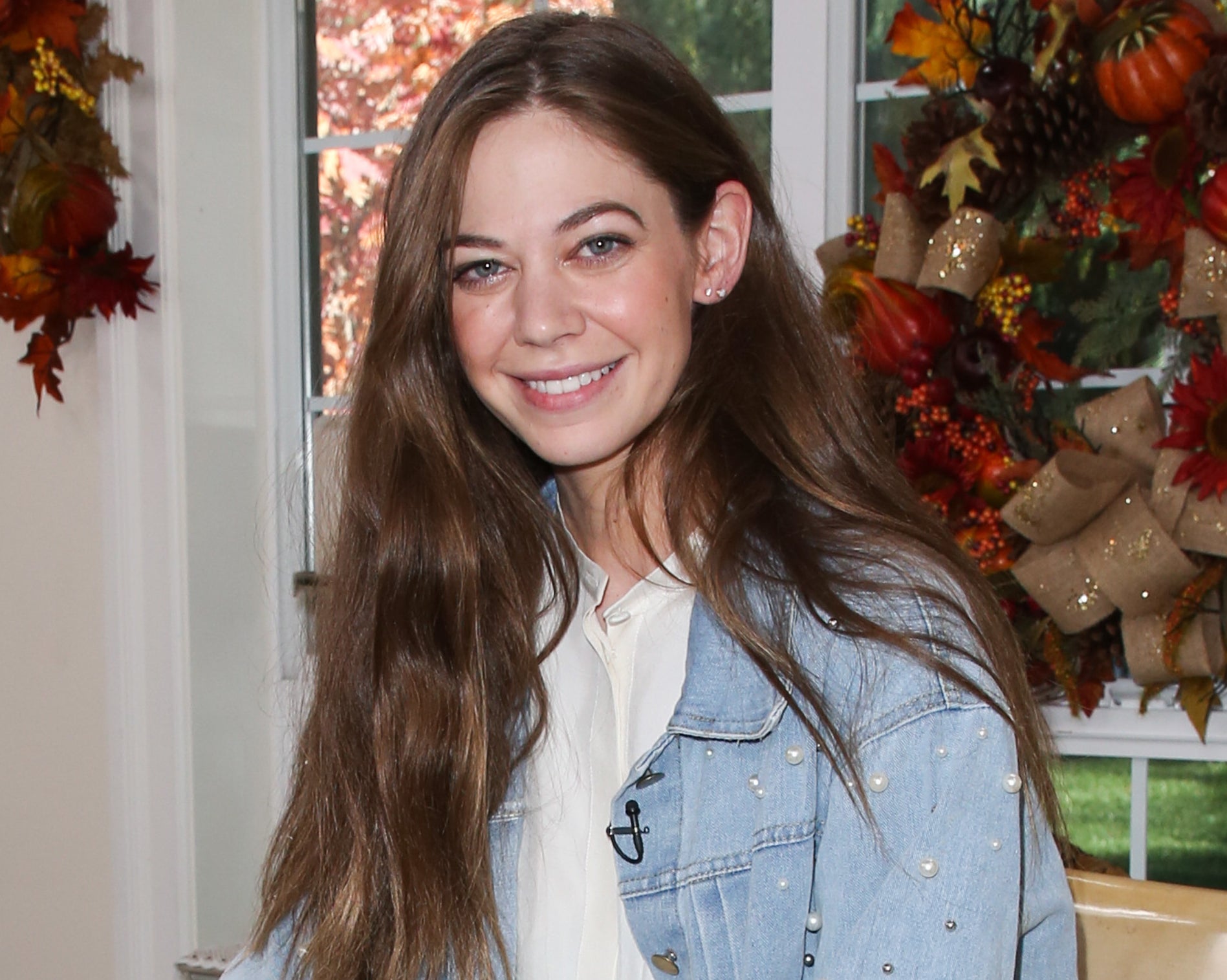 Lio smiles while sitting in a denim jacket with pearl details