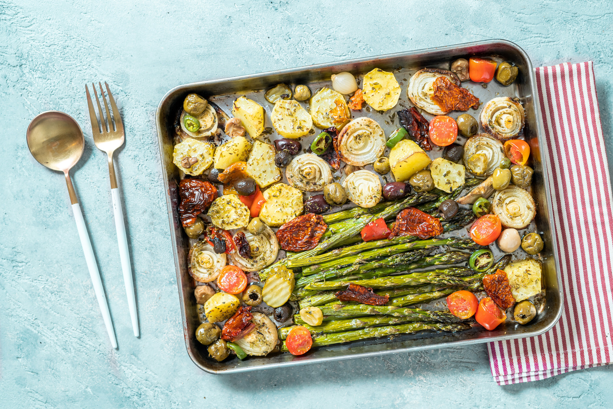 Colorful roasted asparagus, tomatoes, potatoes, and onion on a sheet pan.