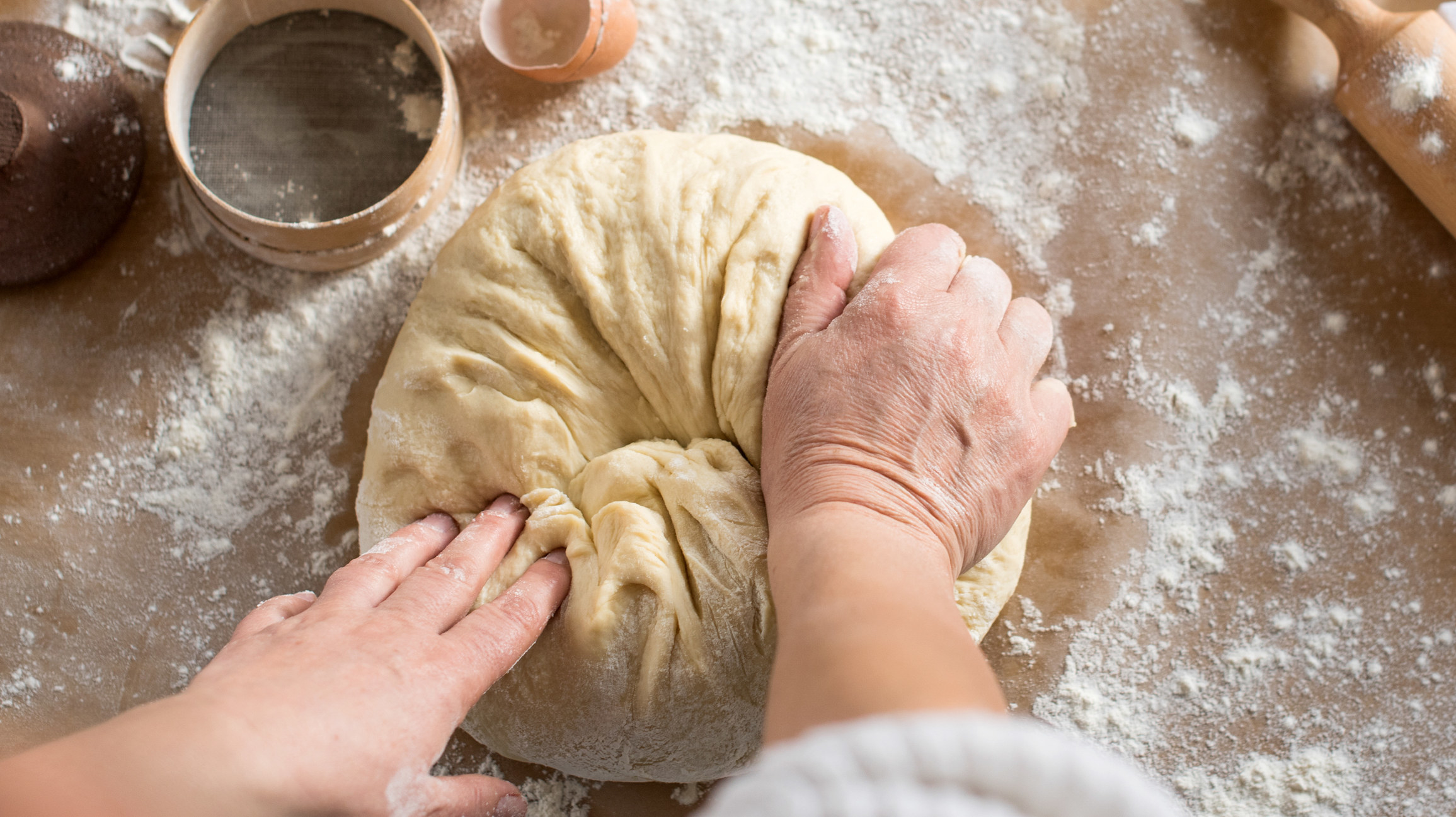 A person kneading pizza dough on a floured surface.
