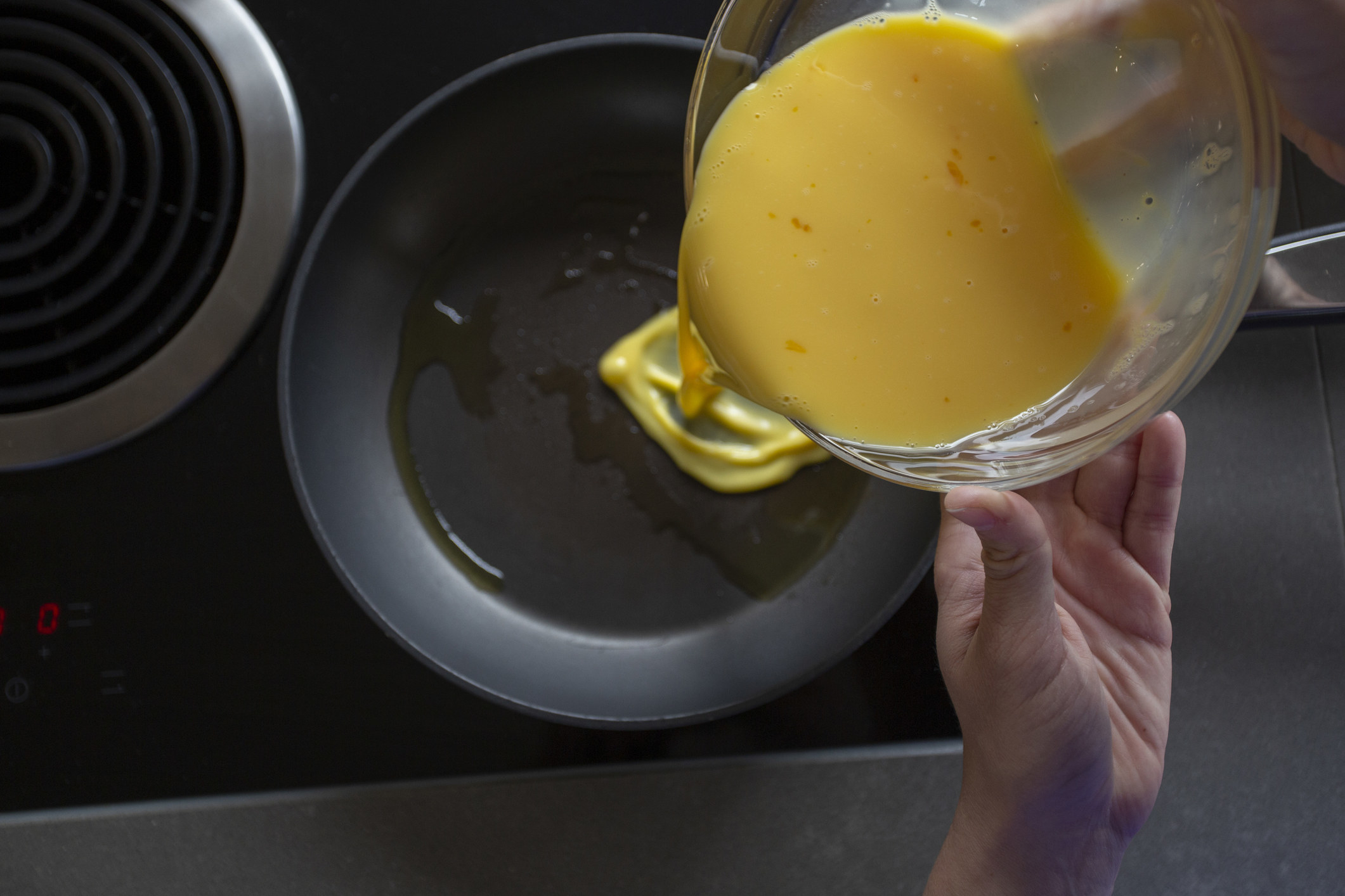 Pouring a beaten egg mixture into a frying pan.