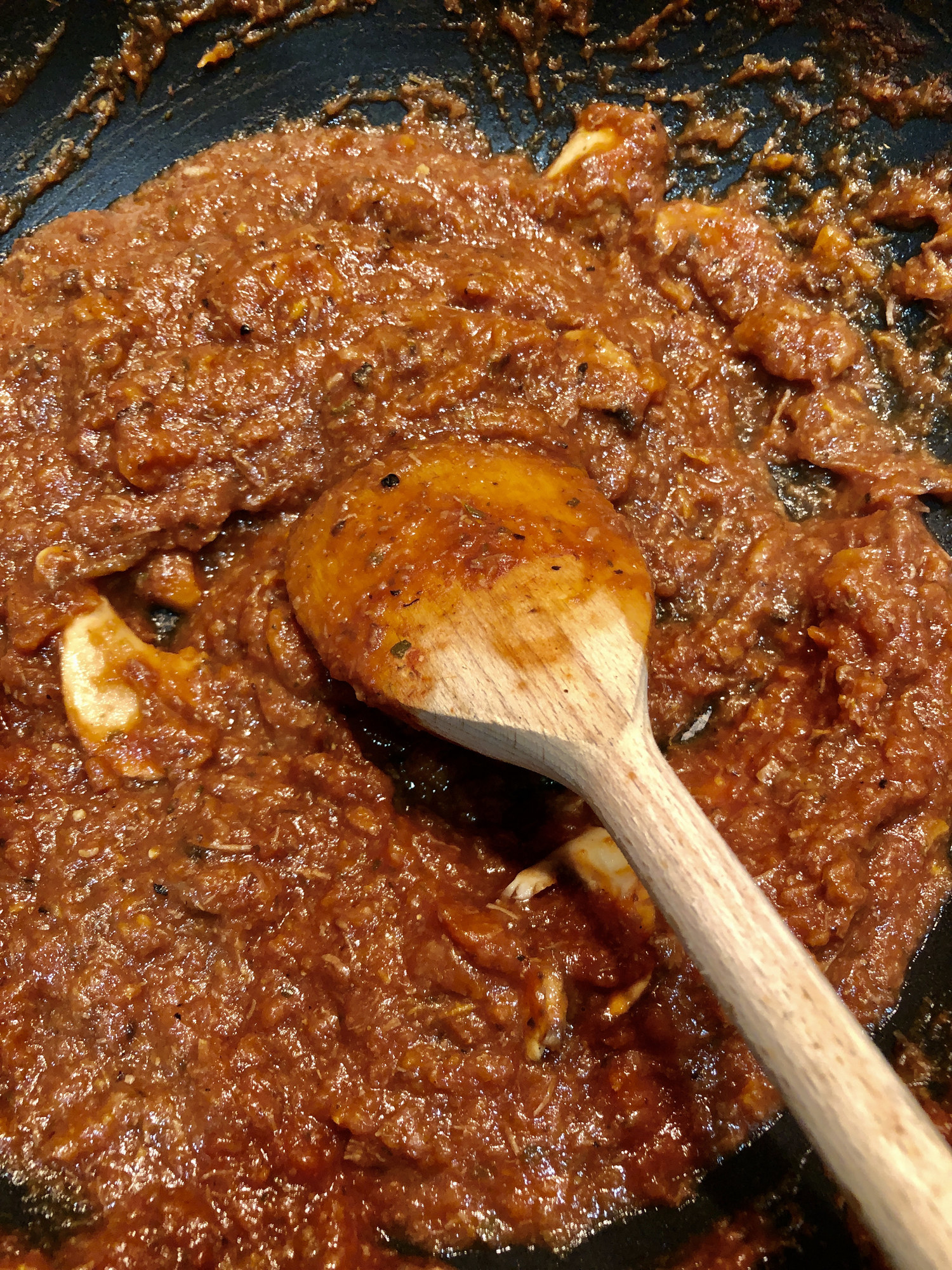 Stirring ragu in a skillet with a wooden spoon.