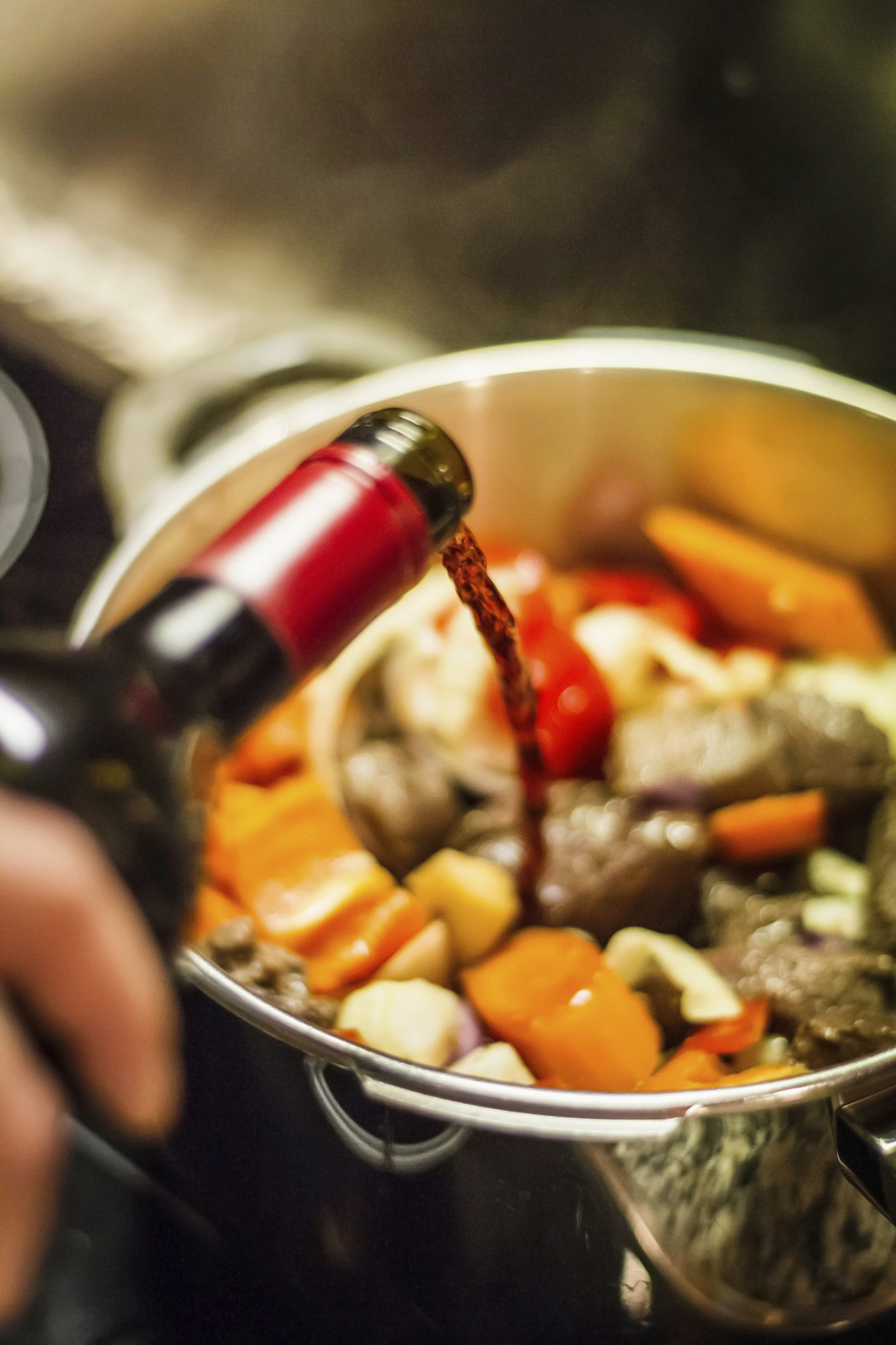 Someone pouring wine into a pot of beef stew.