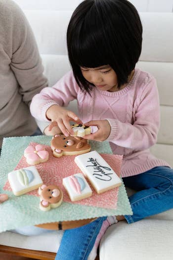 child decorating cookies with a patterned beeswax wrap underneath as a placemat