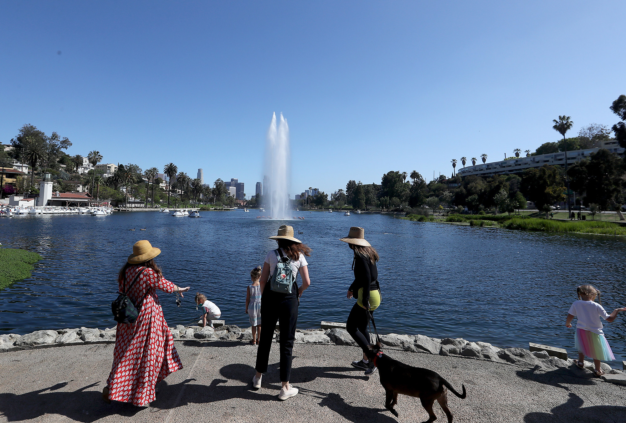 Three women in hats in front of a human-made fountain and a lake