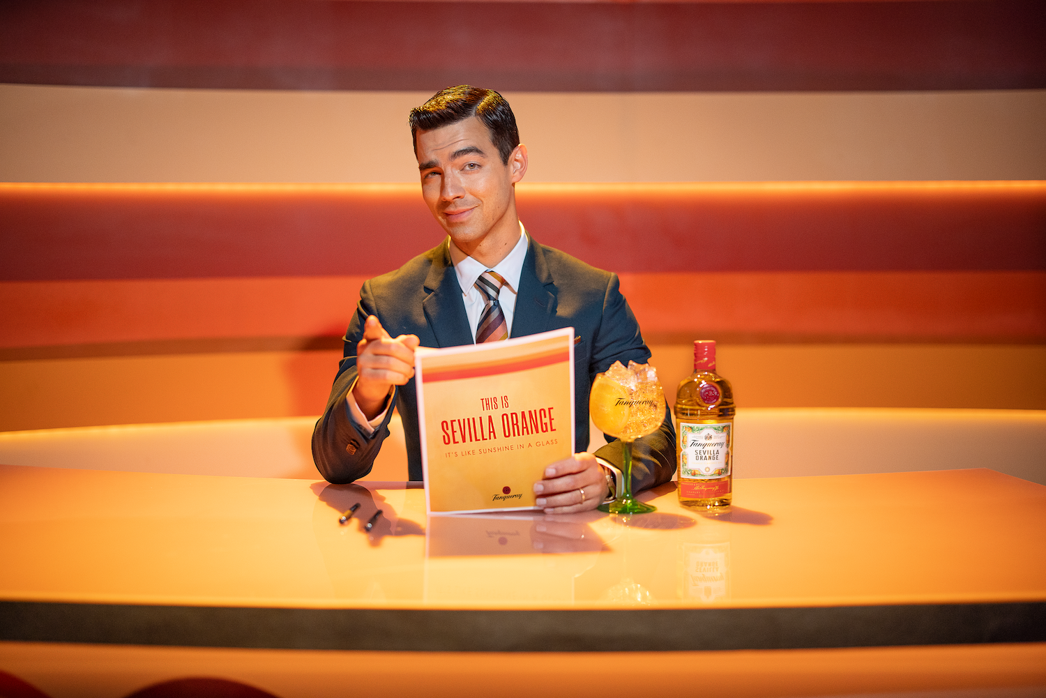 Joe Jonas sitting behind a desk in his content spot for Tanqueray Sevulla Orange