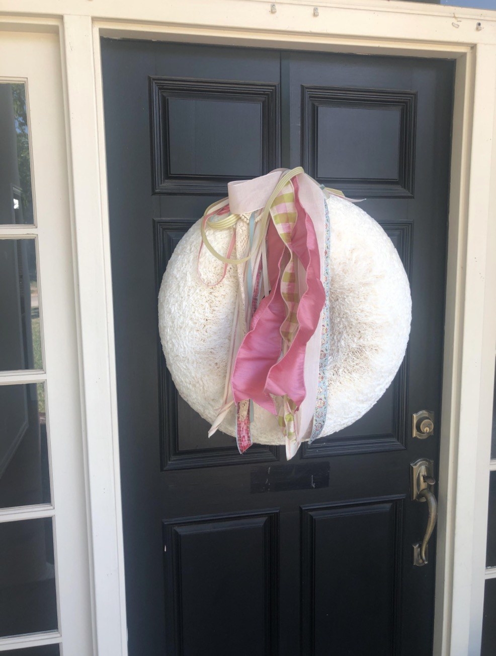 A large, pillowy-looking round white wreath with pink and white tassels and ribbons hanging in the middle hangs on a door