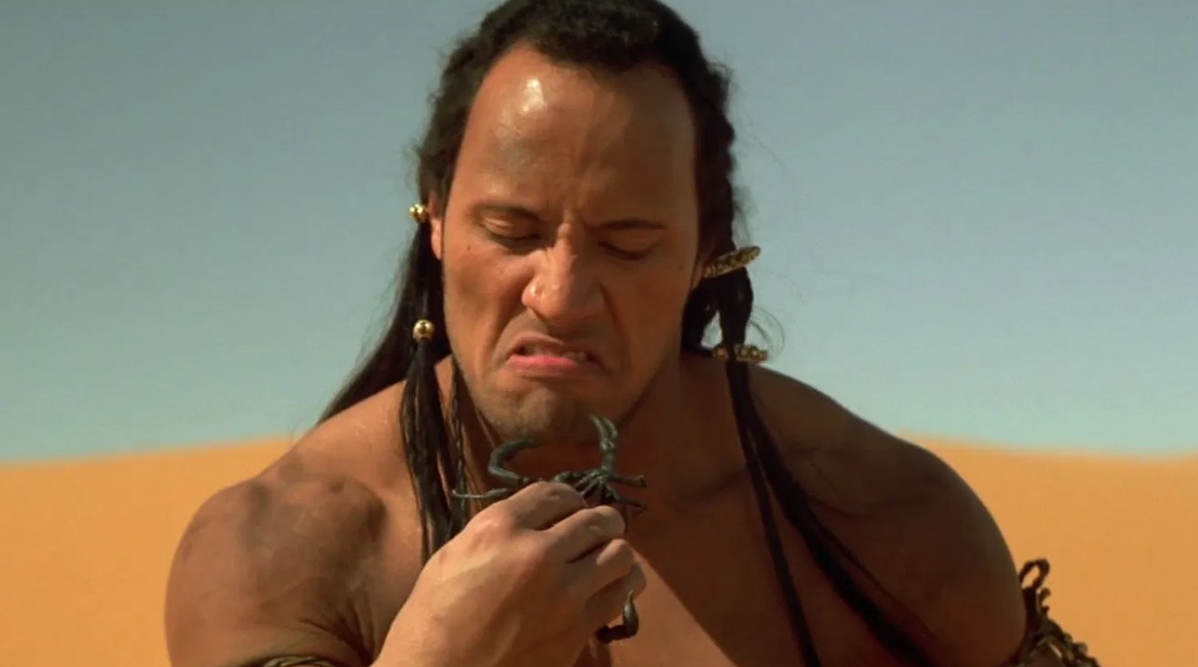 The Scorpion King screwing up his face while looking at the scorpion he&#x27;s holding in his hand