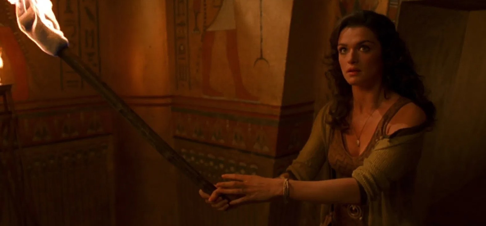 Evie stands in a chamber with hieroglyphics on the walls and holds a fire torch