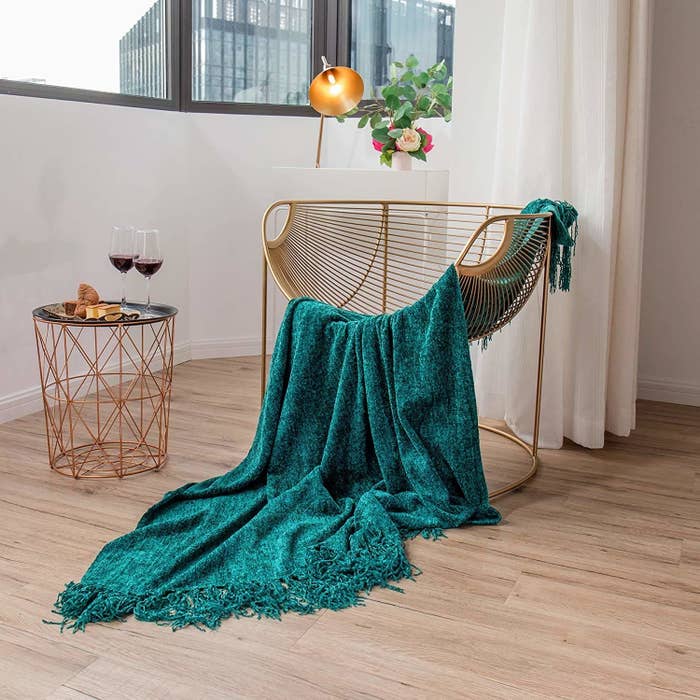 A teal throw blanket on a chair next to a table with wine glasses 