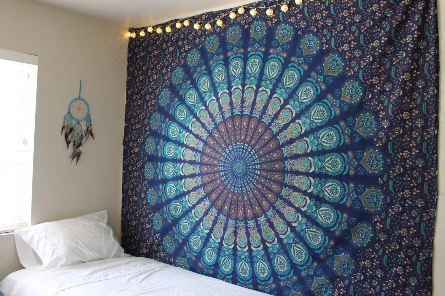 A blue Mandala tapestry on a wall next to a bed and a dreamcatcher 