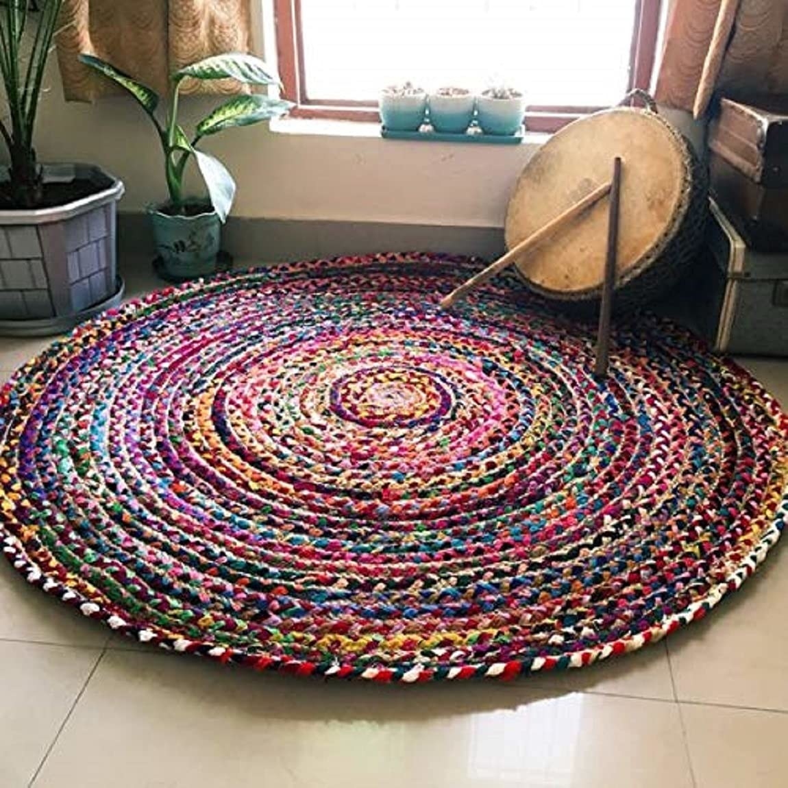 A colourful circular rug on the floor next to some plants 