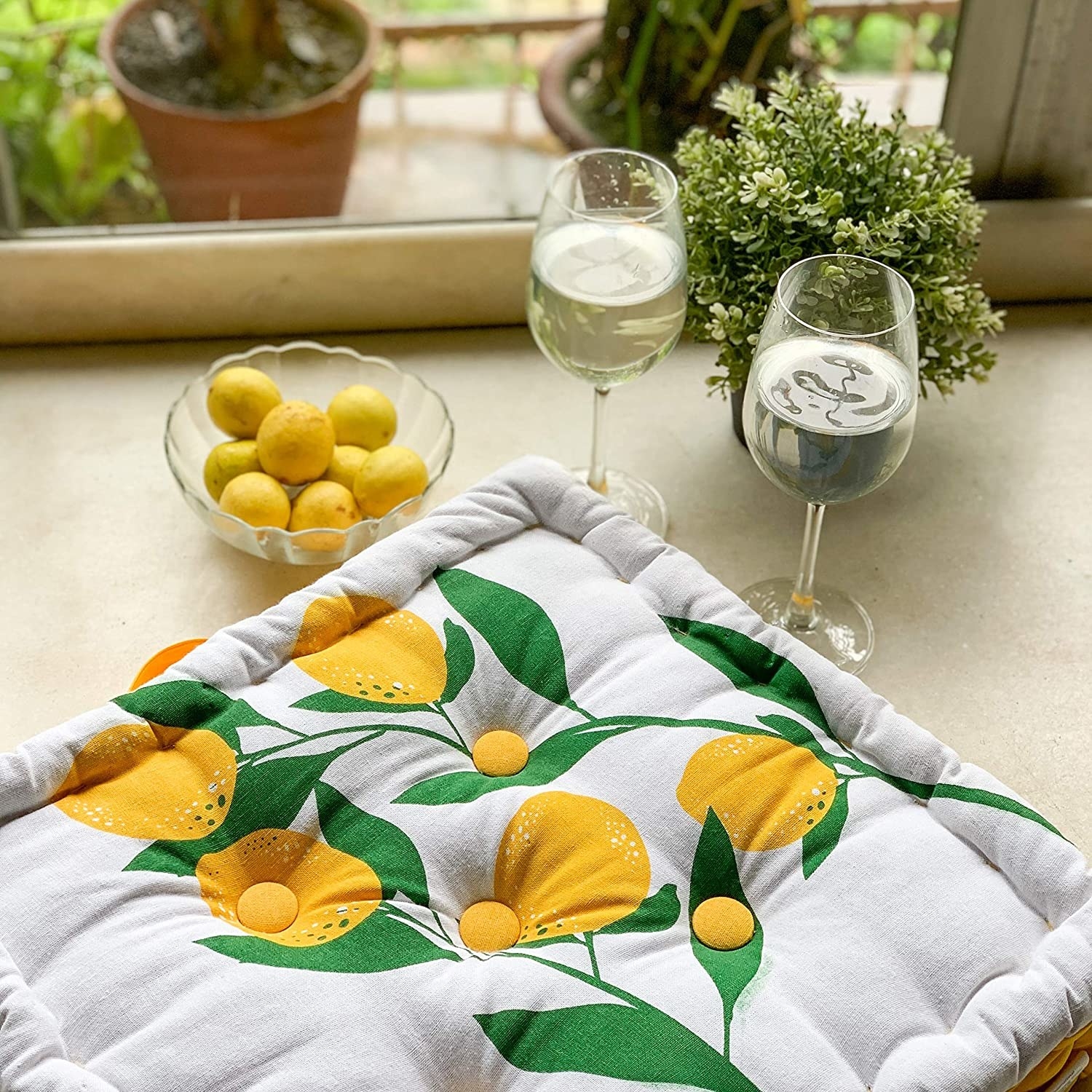 A white and yellow floor cushion with lemons and a glass of wine beside it