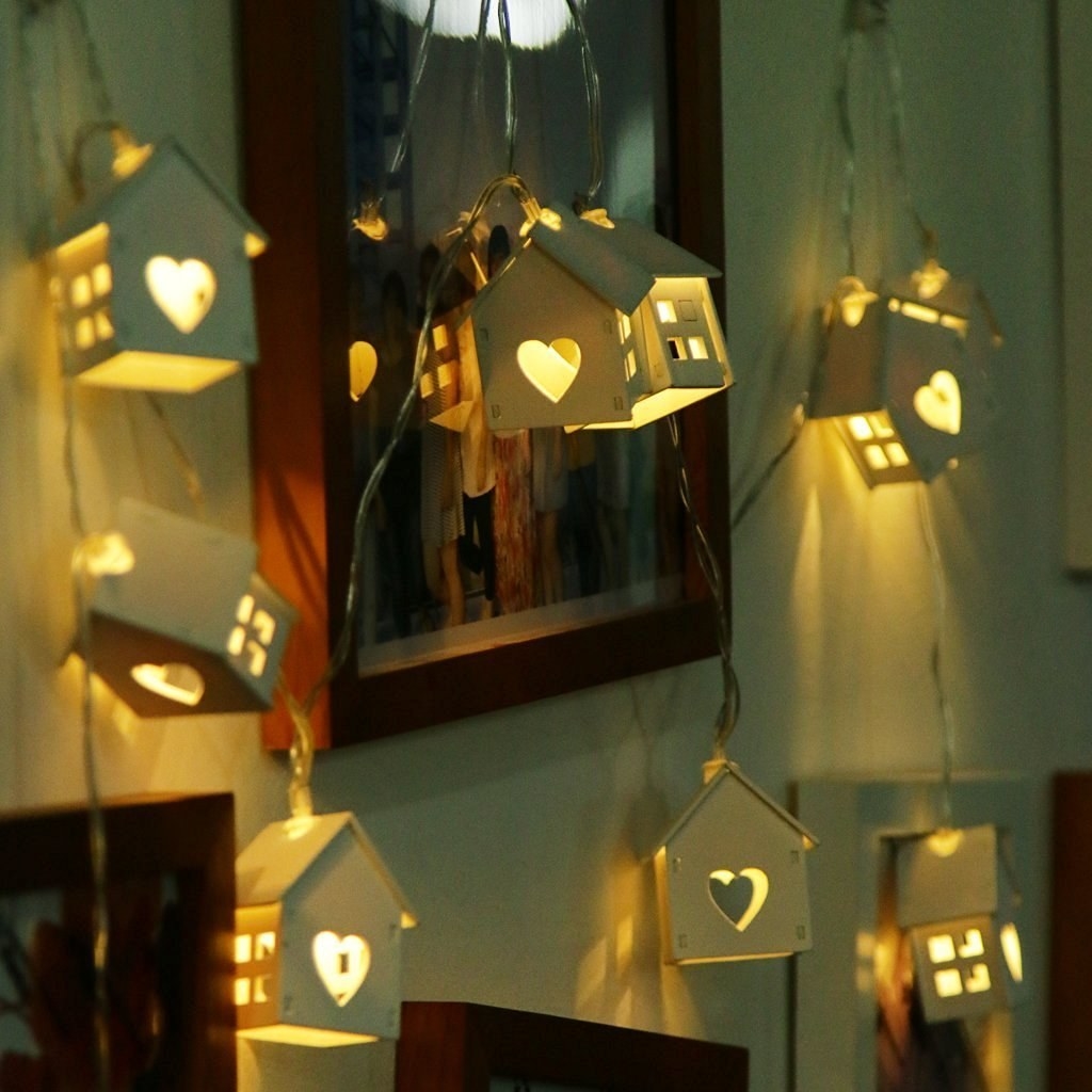 A string of home-shaped lights with hearts in them next to photo frames 