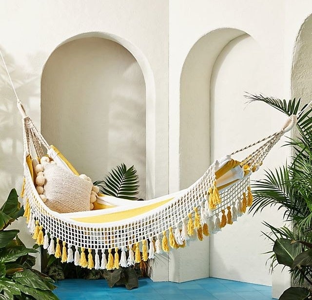 A yellow and white striped hammock with macrame and tassel details