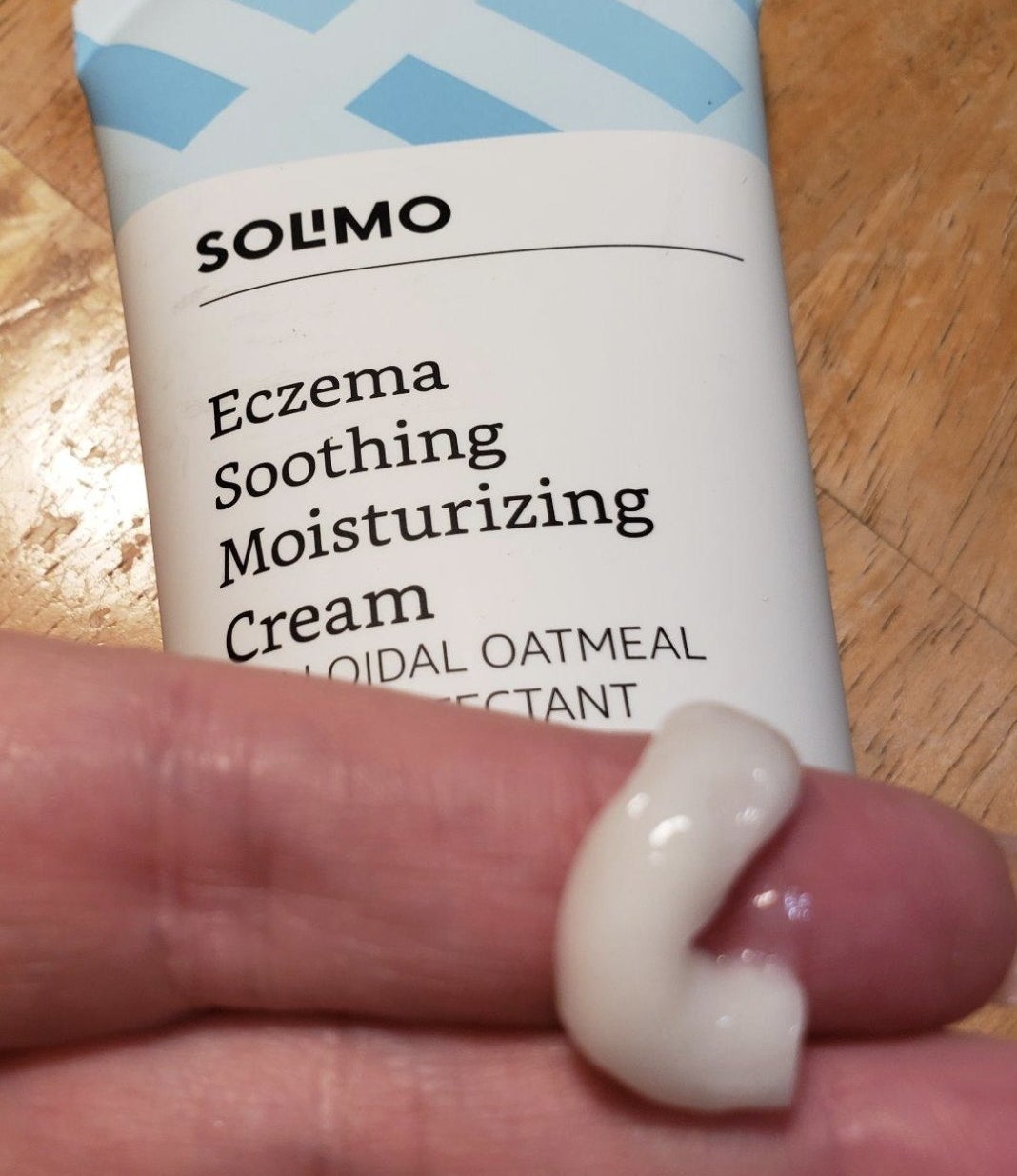 reviewer showing tube of cream as well as a small sample on their finger showing texture/consistency 