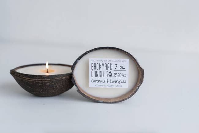 A lit candle in the coconut candle is next to a coconut candle still wrapped and with its packaging on