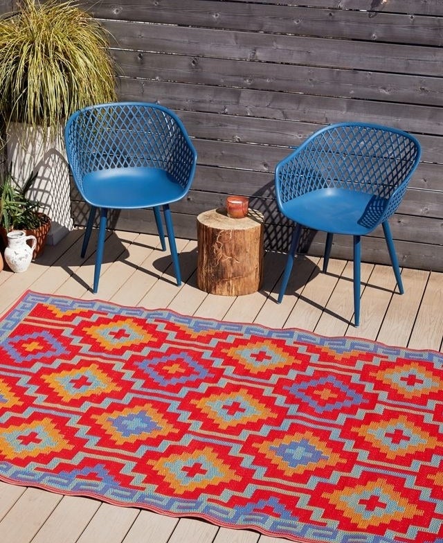 The red and blue rug is displayed outside next to some patio chairs